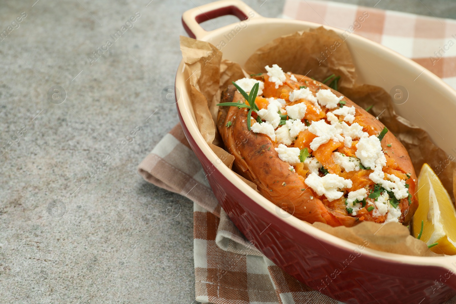 Photo of Tasty baked sweet potato with feta cheese and herbs on grey textured table, closeup. Space for text