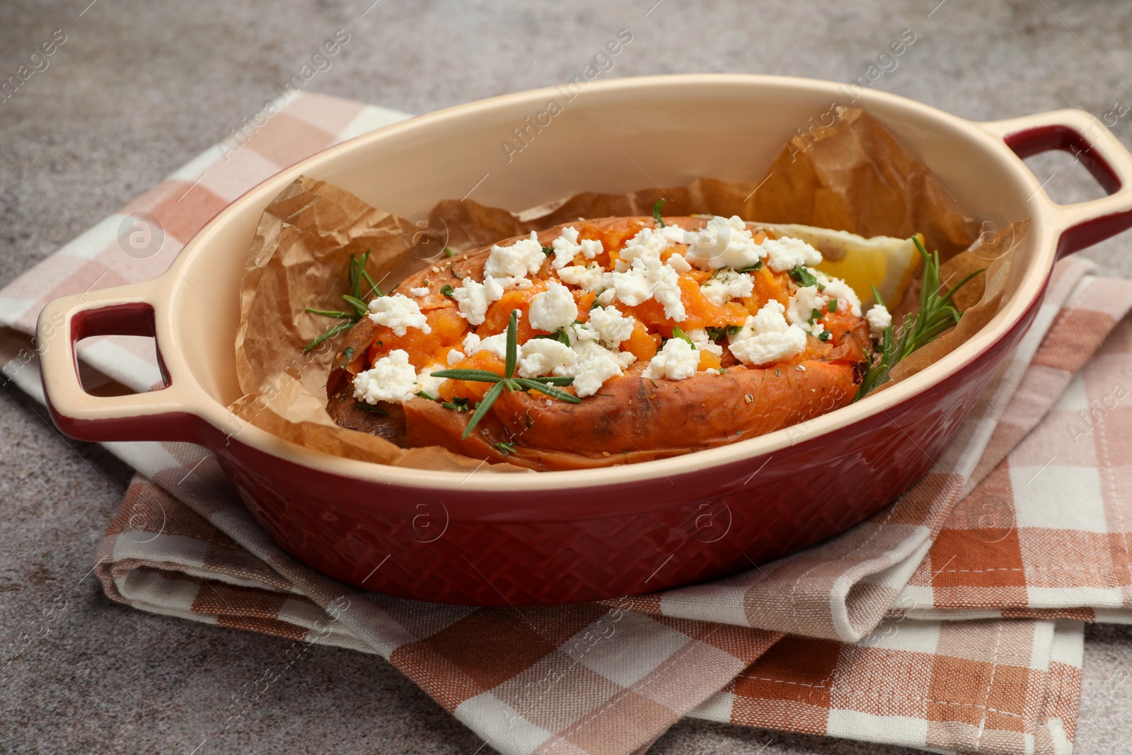 Photo of Tasty baked sweet potato with feta cheese and herbs on grey textured table, closeup