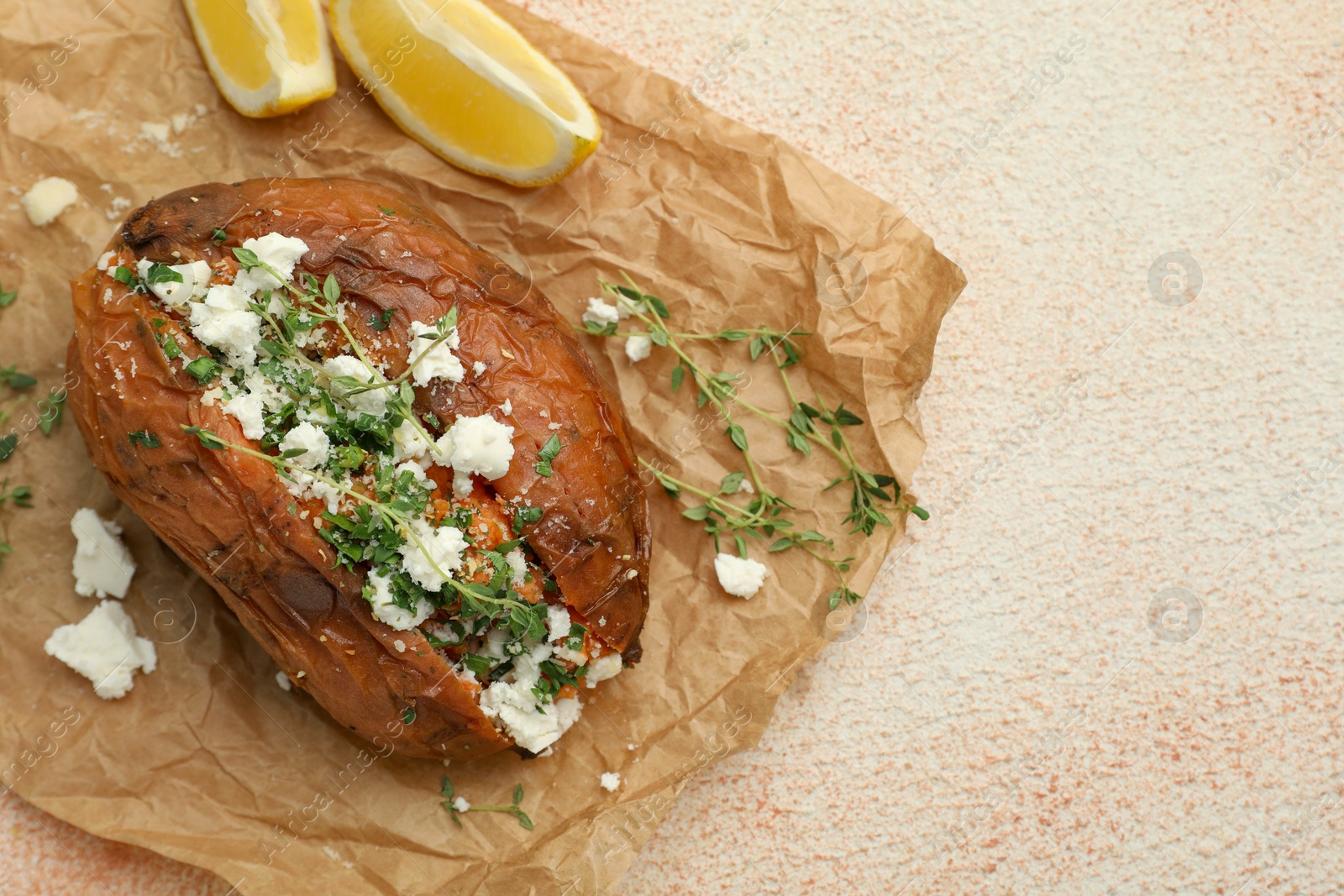 Photo of Tasty baked sweet potato with feta cheese, lemon and herbs on light textured table, top view. Space for text