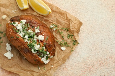 Tasty baked sweet potato with feta cheese, lemon and herbs on light textured table, top view. Space for text