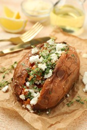 Photo of Tasty baked sweet potato with feta cheese and herbs on light textured table, closeup