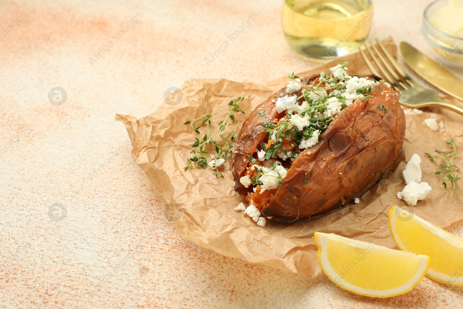 Photo of Tasty baked sweet potato with feta cheese, lemon and herbs on light textured table, closeup. Space for text