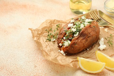 Tasty baked sweet potato with feta cheese, lemon and herbs on light textured table, closeup. Space for text