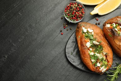 Photo of Tasty baked sweet potato with feta cheese, lemon, peppercorns and herbs on dark textured table, flat lay. Space for text