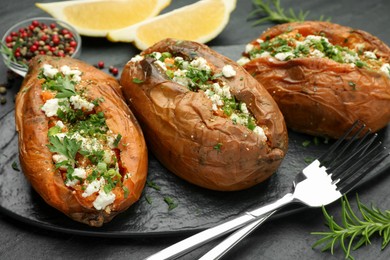 Photo of Tasty baked sweet potato with feta cheese and herbs on dark textured table, closeup