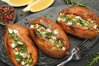 Photo of Tasty baked sweet potato with feta cheese, lemon, peppercorns and herbs on dark textured table, flat lay