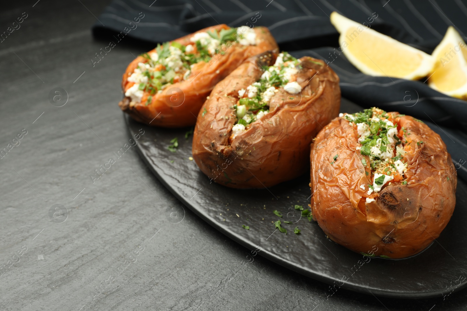 Photo of Tasty baked sweet potato with feta cheese and herbs on dark textured table, closeup. Space for text