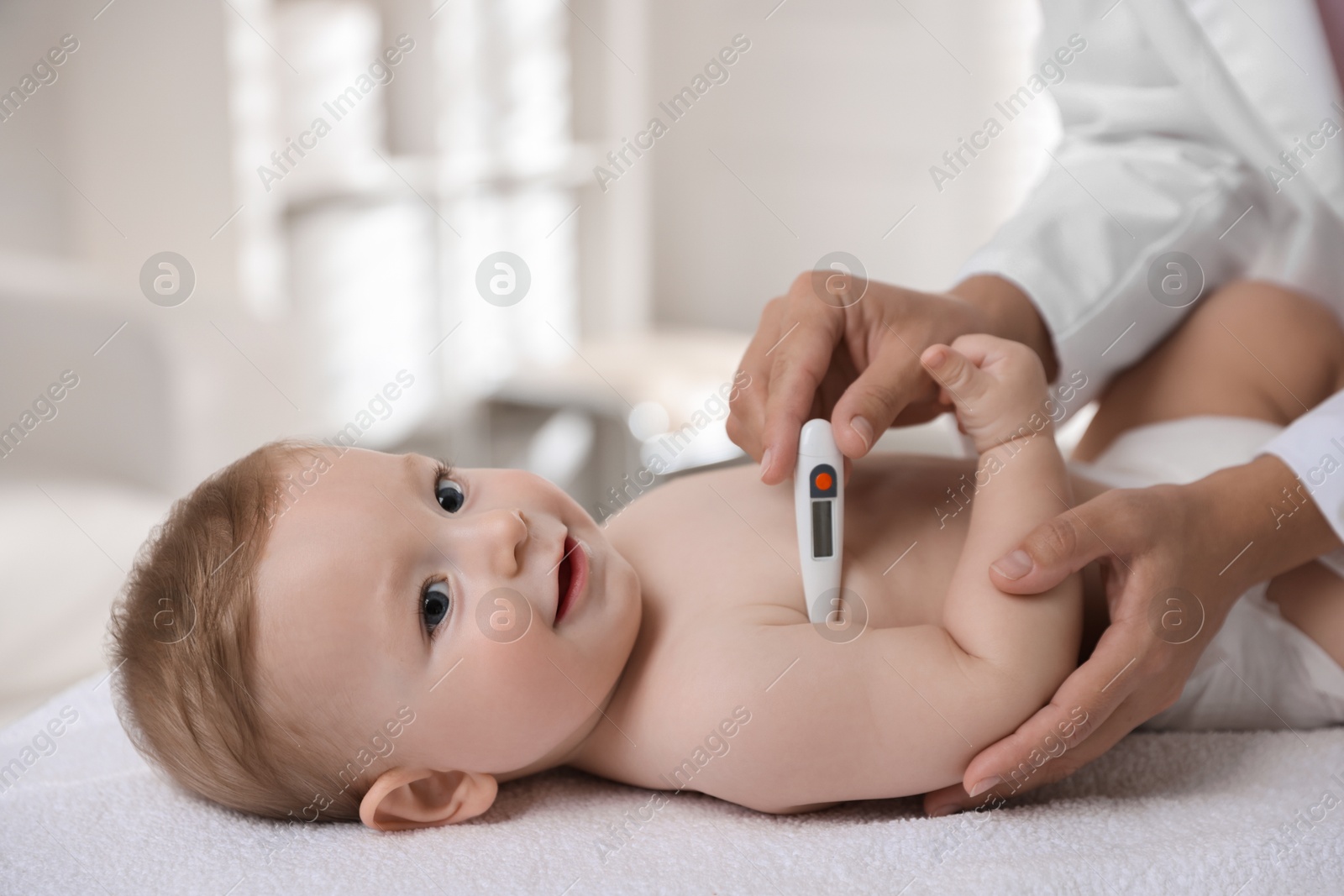 Photo of Pediatrician examining little child with thermometer in clinic, closeup. Checking baby's health