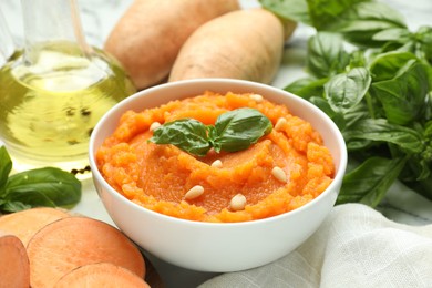 Photo of Tasty mashed sweet potato with basil, seeds in bowl and ingredients on white table, closeup