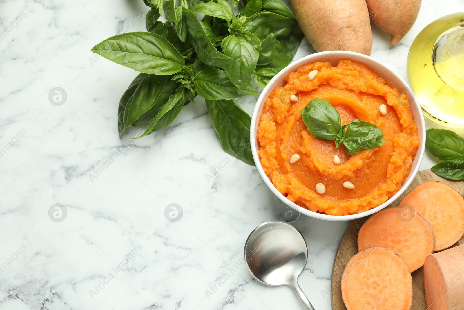 Photo of Tasty mashed sweet potato with basil, seeds in bowl and fresh vegetables on white marble table, flat lay. Space for text