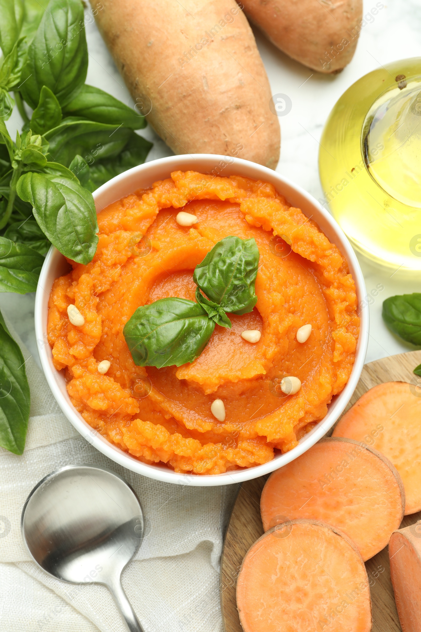 Photo of Tasty mashed sweet potato with basil, seeds in bowl and fresh vegetables on white table, flat lay