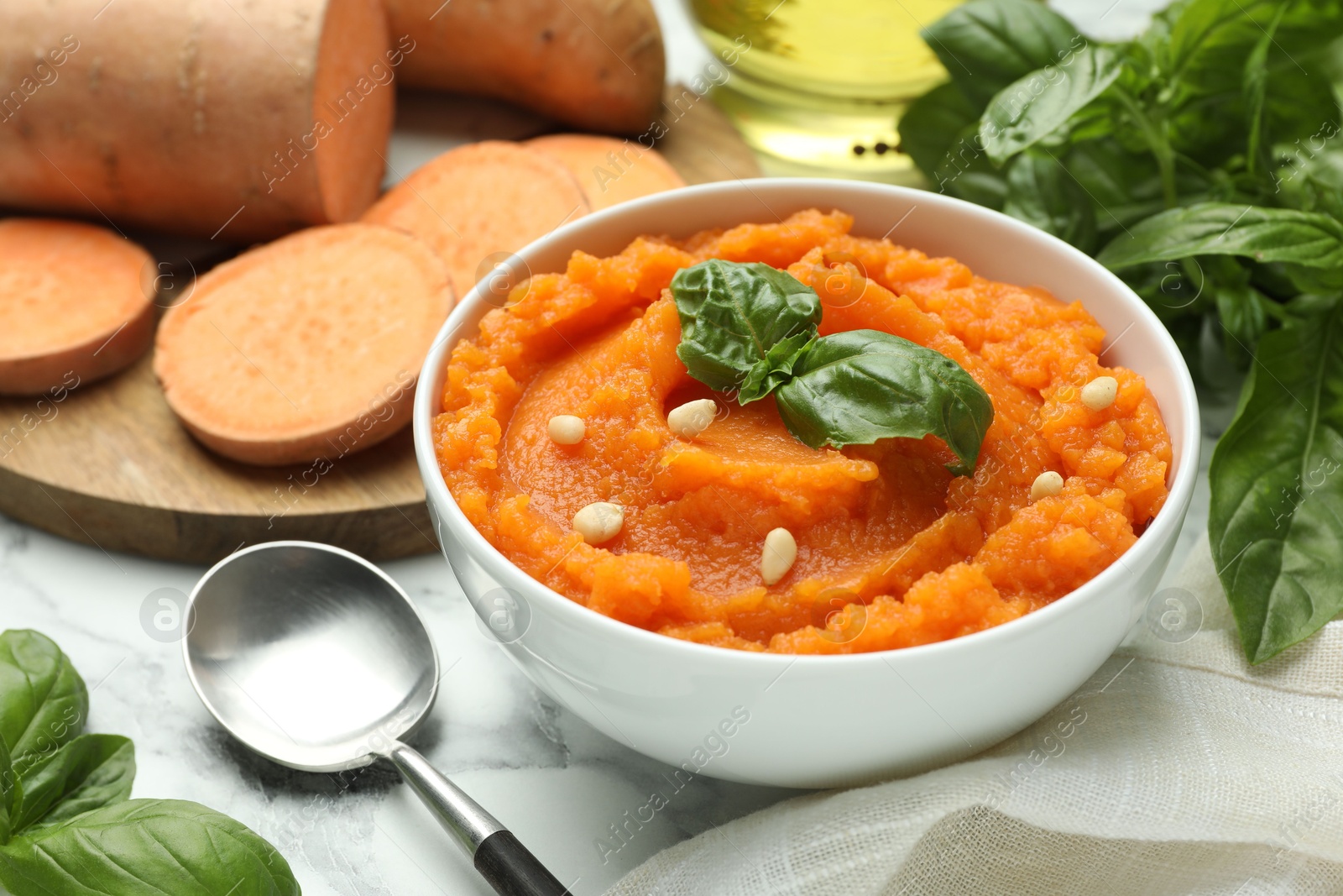 Photo of Tasty mashed sweet potato with basil, seeds in bowl and ingredients on table, closeup