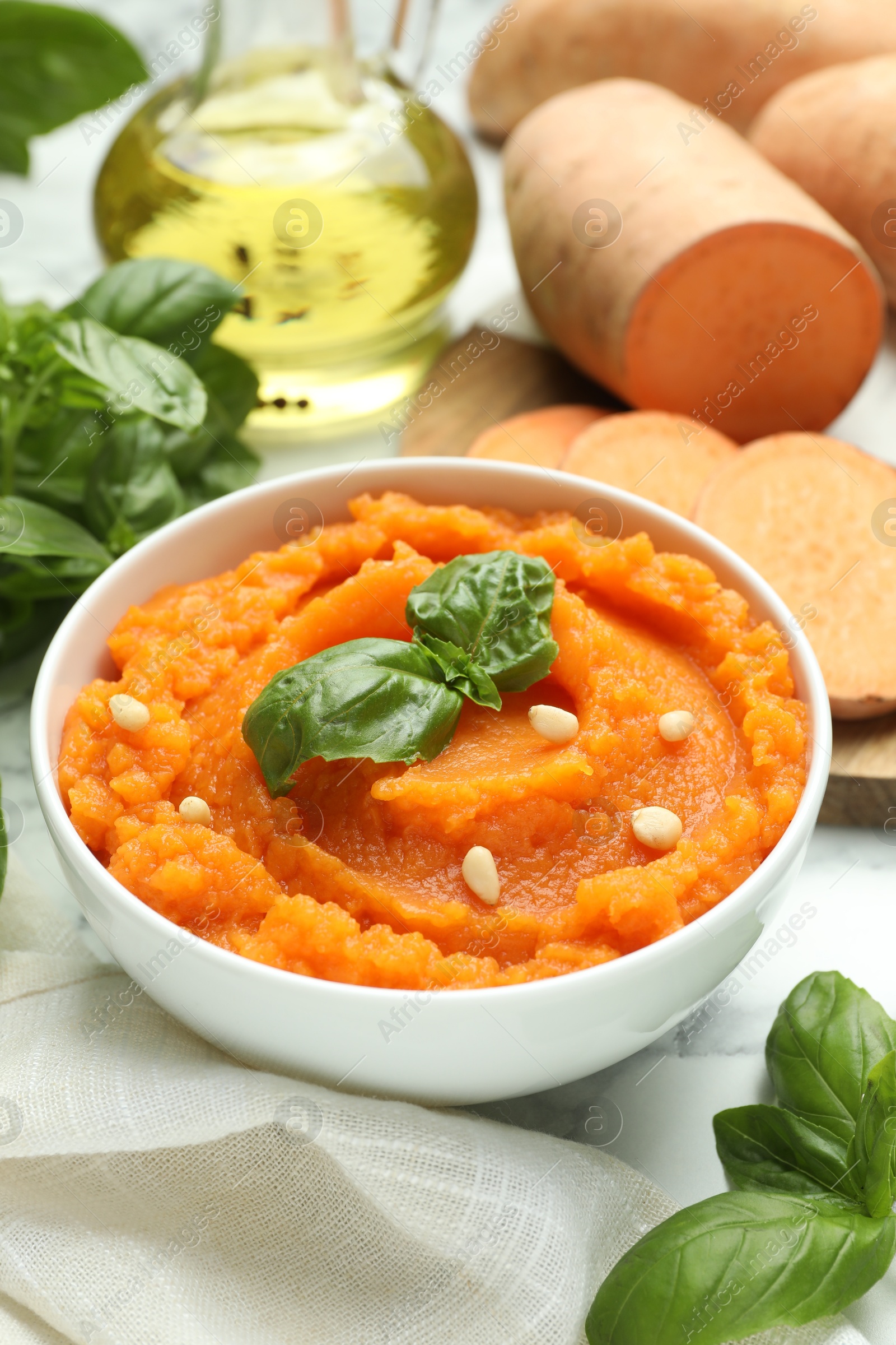 Photo of Tasty mashed sweet potato with basil, seeds in bowl and ingredients on table, closeup