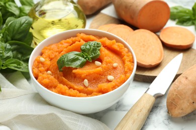 Photo of Tasty mashed sweet potato with basil, seeds in bowl and ingredients on table, closeup