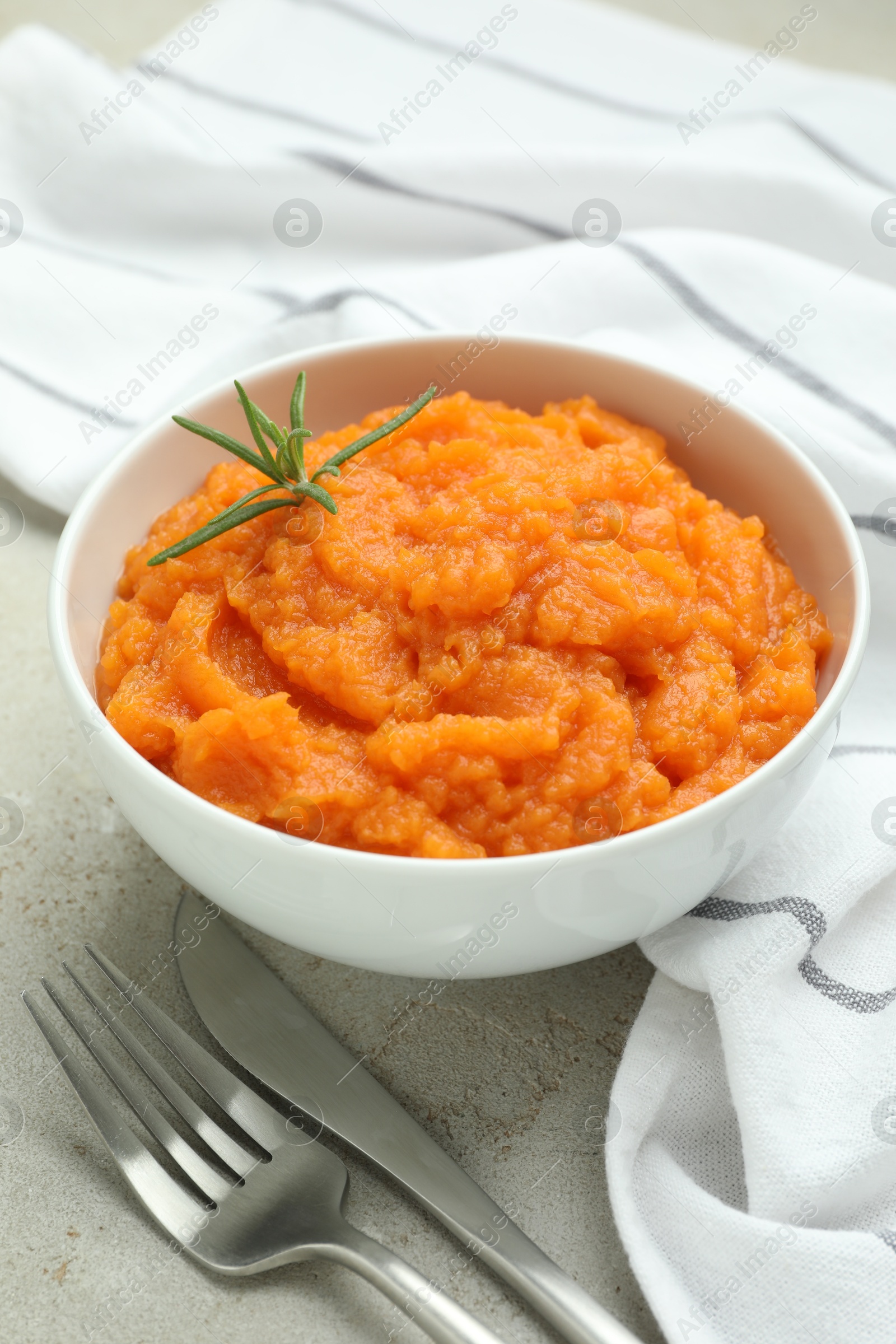 Photo of Tasty mashed sweet potato with rosemary in bowl served on grey textured table, closeup