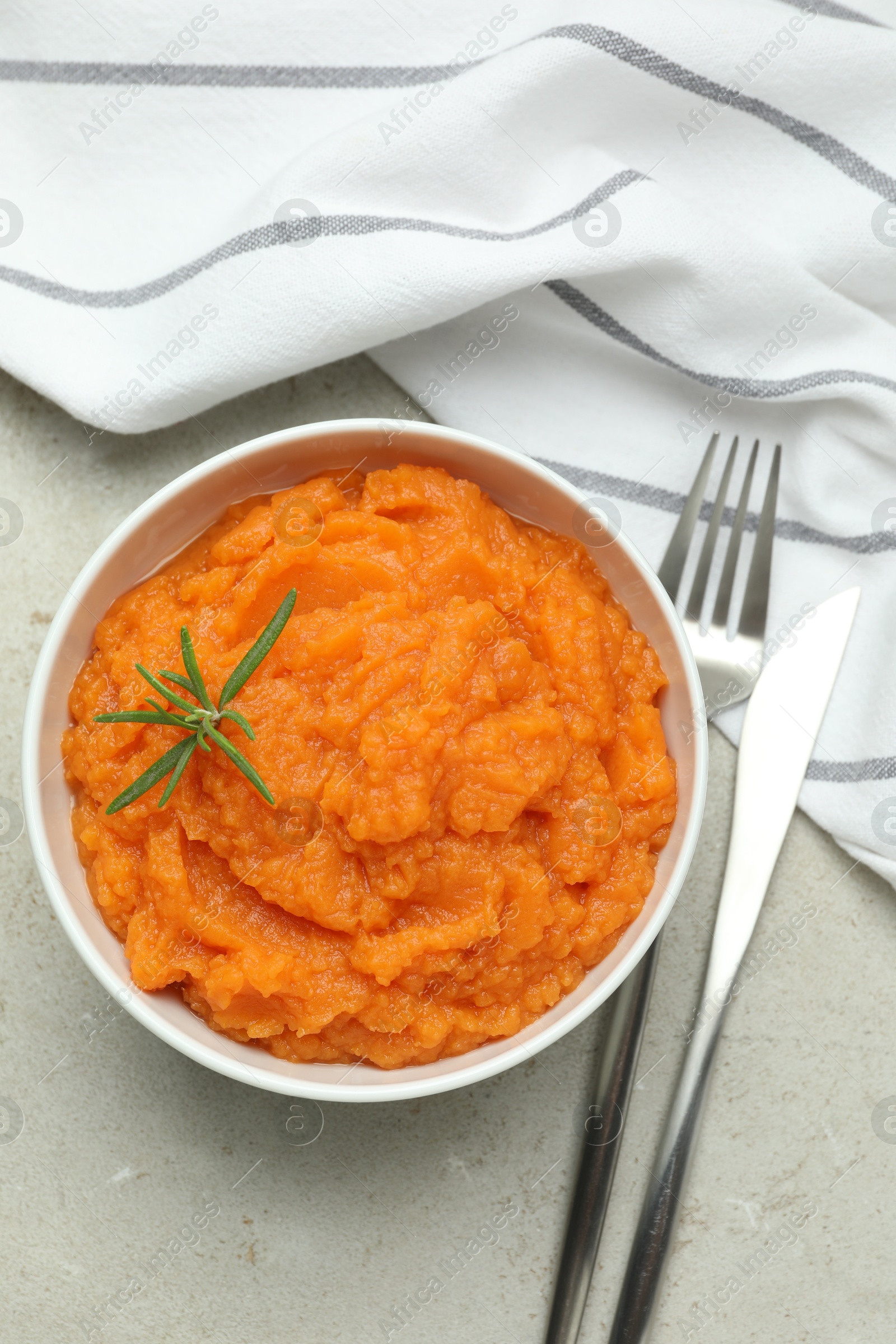 Photo of Tasty mashed sweet potato with rosemary in bowl served on grey textured table, flat lay