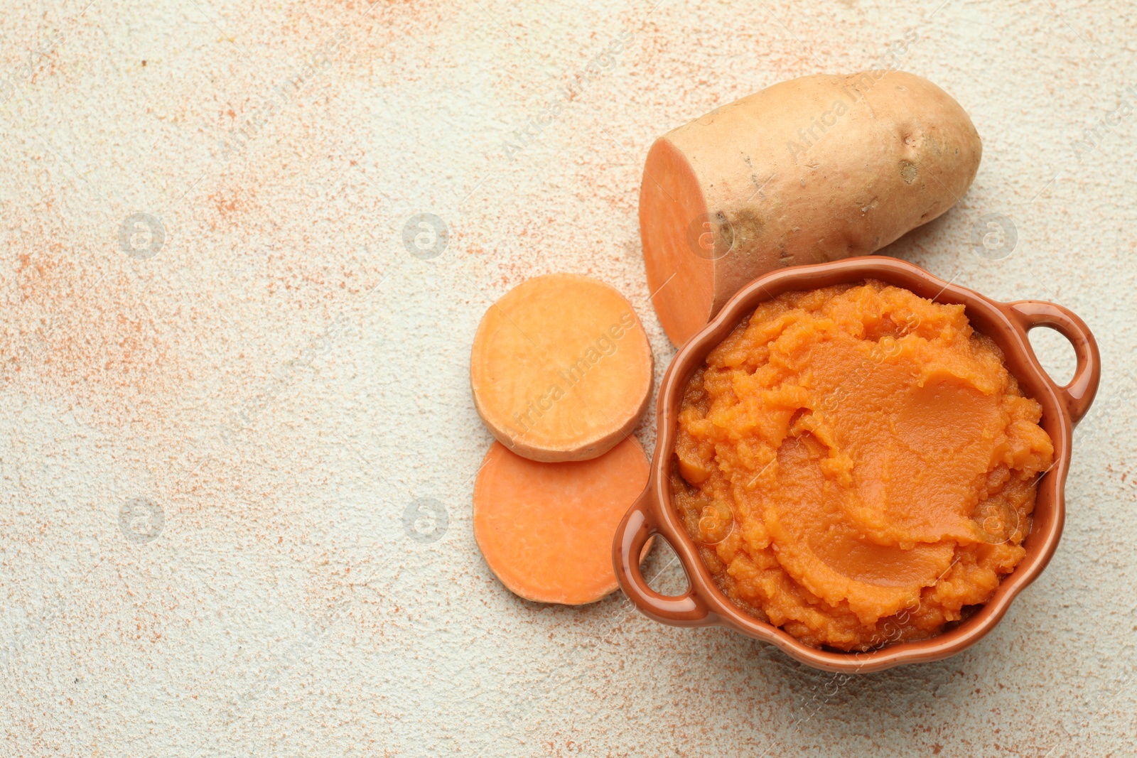 Photo of Tasty mashed sweet potato in bowl and cut vegetable on beige textured table, flat lay. Space for text