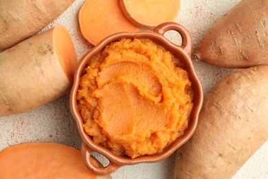 Photo of Tasty mashed sweet potato in bowl and fresh vegetables on beige textured table, flat lay