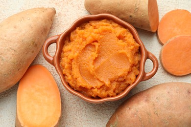 Photo of Tasty mashed sweet potato in bowl and fresh vegetables on beige textured table, flat lay