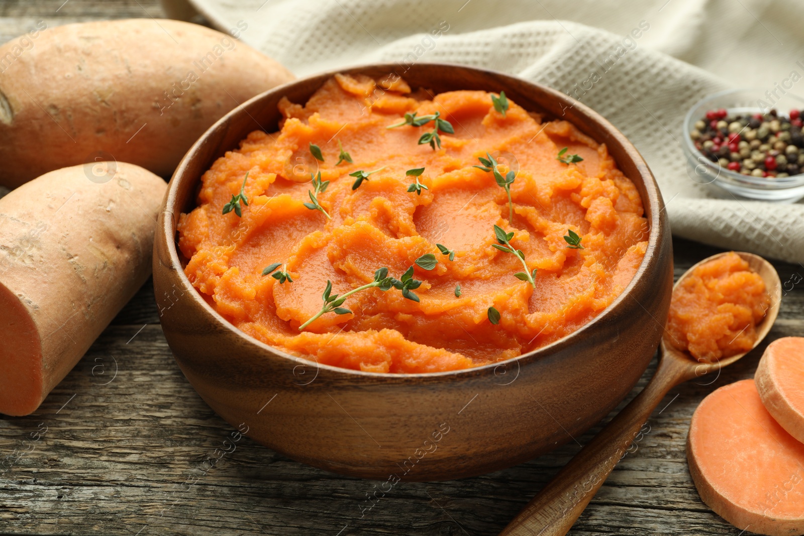 Photo of Tasty mashed sweet potato with thyme in bowl and fresh vegetables on wooden table, closeup