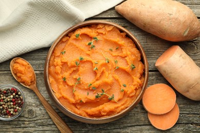 Photo of Tasty mashed sweet potato with thyme in bowl, fresh vegetables and spices on wooden table, flat lay