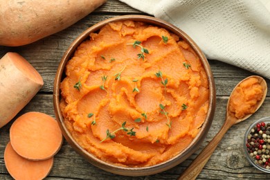 Photo of Tasty mashed sweet potato with thyme in bowl, fresh vegetables and spices on wooden table, flat lay