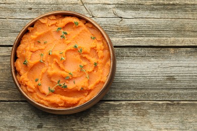 Photo of Tasty mashed sweet potato with thyme in bowl on wooden table, top view. Space for text