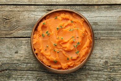 Photo of Tasty mashed sweet potato with thyme in bowl on wooden table, top view