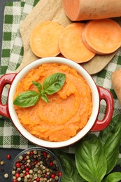 Photo of Tasty mashed sweet potato with basil in pot, cut vegetable and spices on table, flat lay