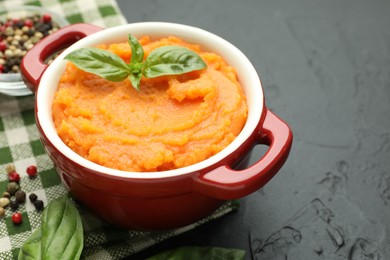 Photo of Tasty mashed sweet potato with basil in pot and spices on dark textured table, closeup