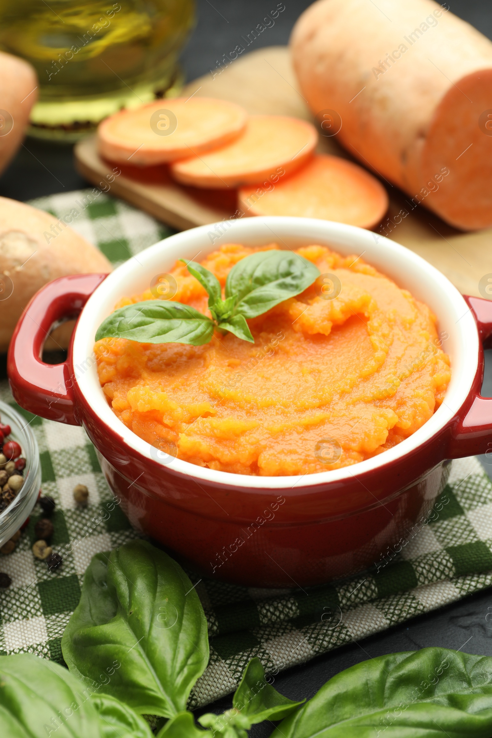 Photo of Tasty mashed sweet potato with basil in pot and fresh vegetables on table, closeup