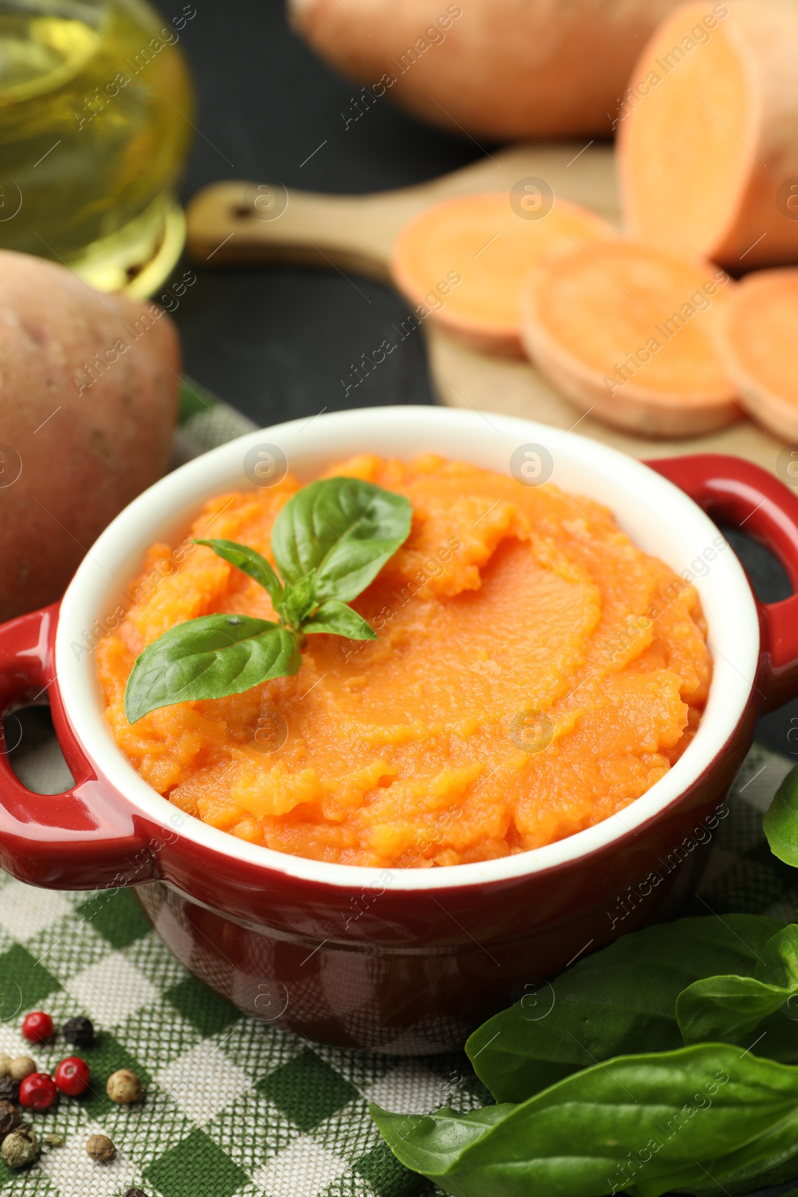 Photo of Tasty mashed sweet potato with basil in, fresh vegetables and spices on table, closeup