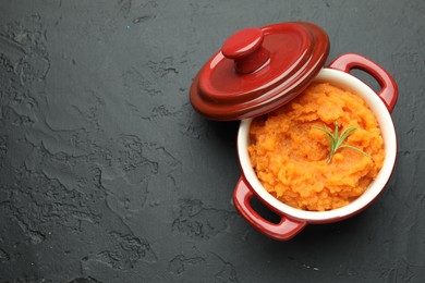 Photo of Tasty mashed sweet potato with rosemary in pot on dark textured table, top view. Space for text