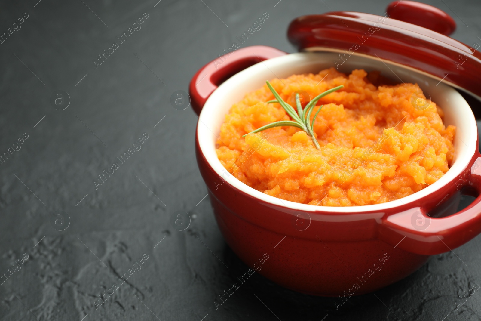 Photo of Tasty mashed sweet potato with rosemary in pot on dark textured table, closeup. Space for text