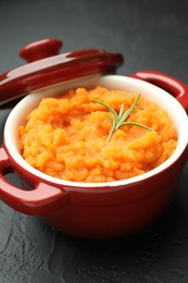 Photo of Tasty mashed sweet potato with rosemary in pot on dark textured table, closeup