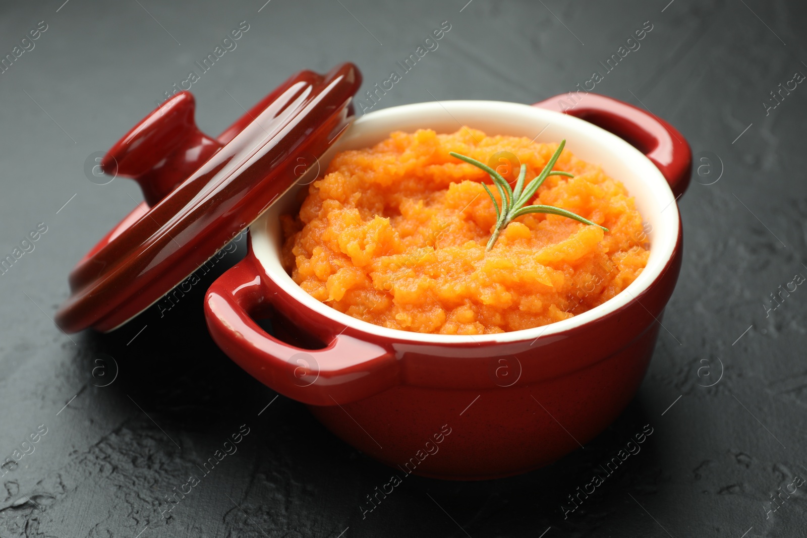 Photo of Tasty mashed sweet potato with rosemary in pot on dark textured table, closeup