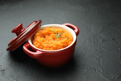 Photo of Tasty mashed sweet potato with rosemary in pot on dark textured table, closeup. Space for text