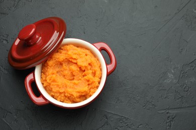 Photo of Tasty mashed sweet potato with rosemary in pot on dark textured table, top view. Space for text