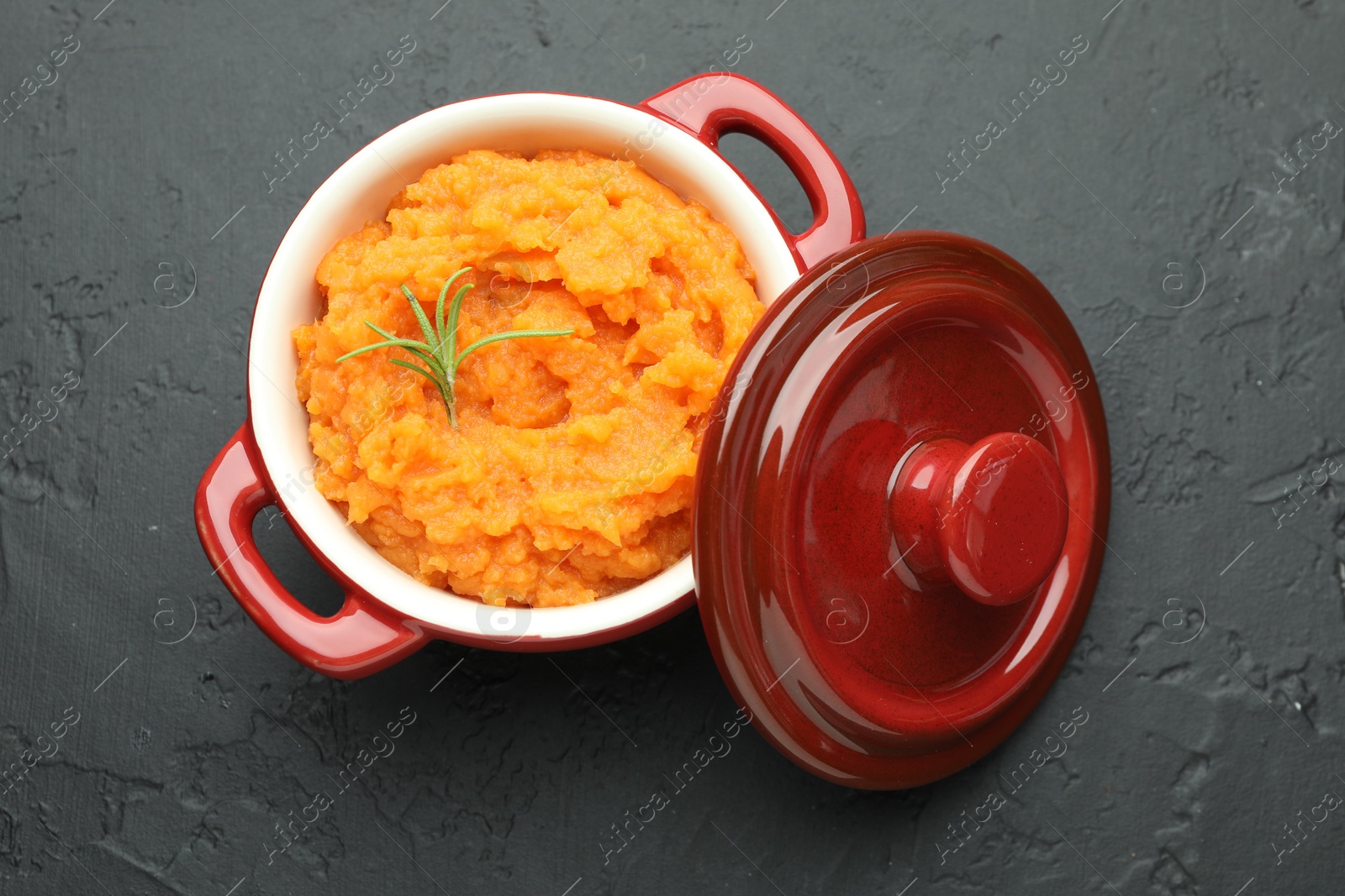 Photo of Tasty mashed sweet potato with rosemary in pot on dark textured table, top view