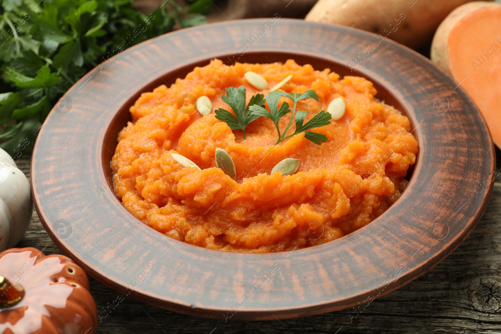 Photo of Tasty mashed sweet potato with pumpkin seeds and parsley in bowl on table, closeup