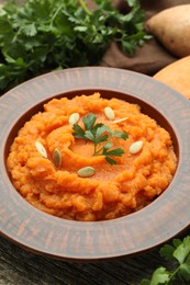 Tasty mashed sweet potato with pumpkin seeds and parsley in bowl on table, closeup