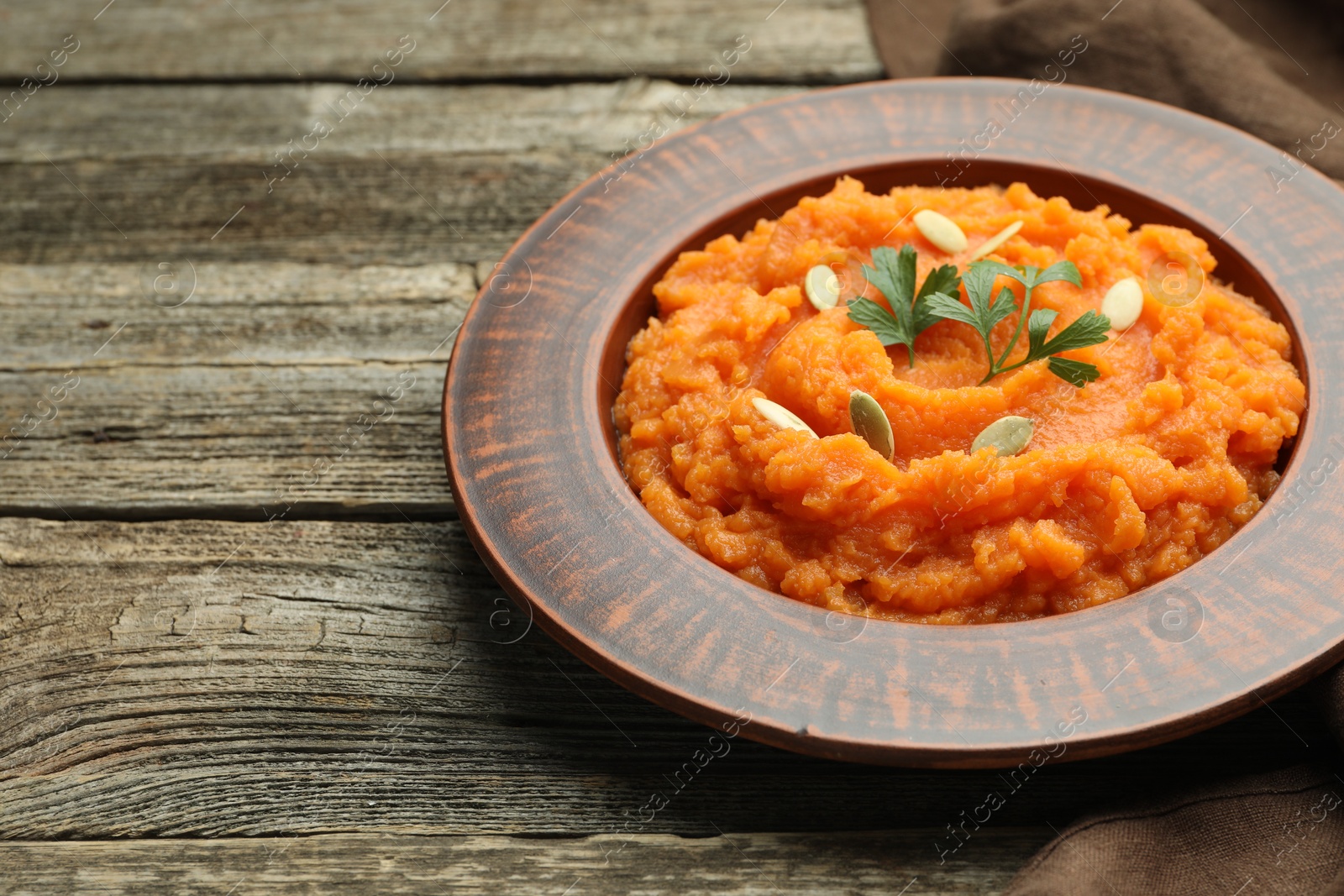 Photo of Tasty mashed sweet potato with pumpkin seeds and parsley in bowl on wooden table, closeup. Space for text