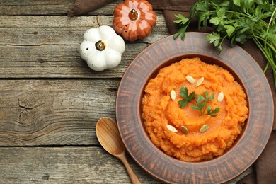 Photo of Tasty mashed sweet potato with pumpkin seeds in bowl, parsley and spices on wooden table, flat lay. Space for text