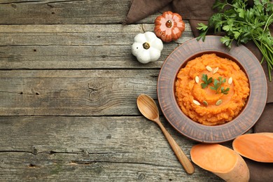 Photo of Tasty mashed sweet potato with pumpkin seeds in bowl, cut vegetable and parsley on wooden table, flat lay. Space for text