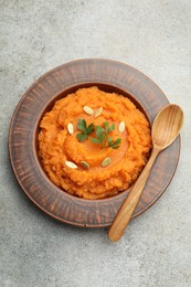 Photo of Tasty mashed sweet potato with pumpkin seeds and parsley in bowl served on gray textured table, top view