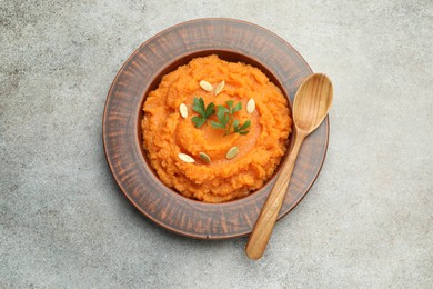 Photo of Tasty mashed sweet potato with pumpkin seeds and parsley in bowl served on gray textured table, top view