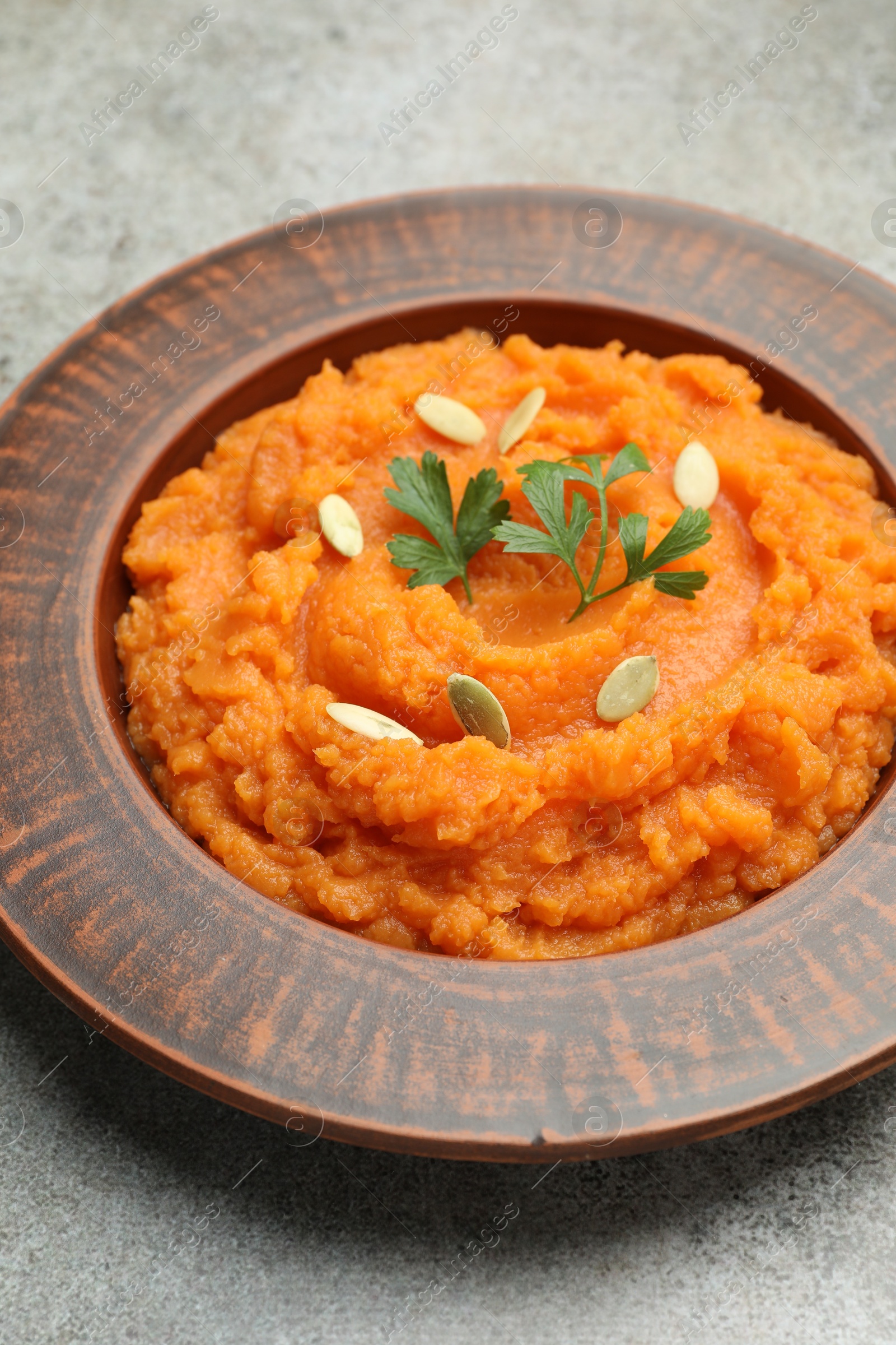 Photo of Tasty mashed sweet potato with pumpkin seeds and parsley in bowl on gray textured table, closeup