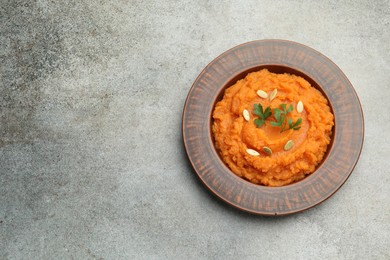 Photo of Tasty mashed sweet potato with pumpkin seeds and parsley in bowl on gray textured table, top view. Space for text