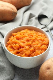 Photo of Tasty mashed sweet potato in bowl and fresh vegetables on gray table, closeup