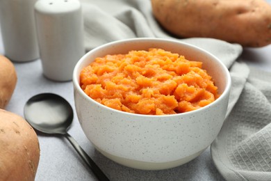 Photo of Tasty mashed sweet potato in bowl, spoon and fresh vegetables on gray table, closeup